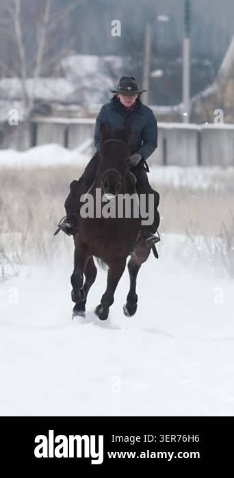 Woman in cawboy hat galloping on big dark horse in snow field - slow ...