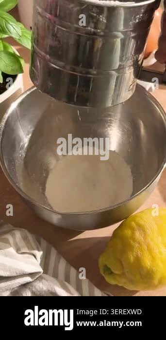 Baker sifting flour with a stainless steel sifter into a metal bowl to ...