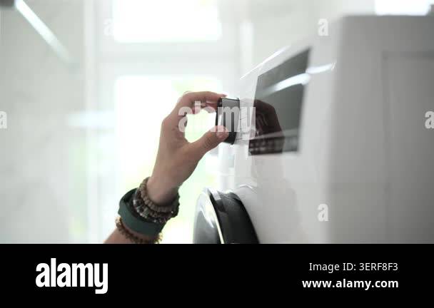 Persons hand adjusts dial on modern white washing machine panel ...