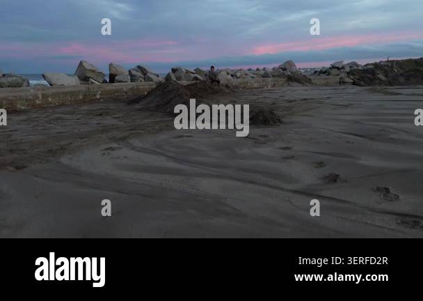 Two young boys play on a sandy beach near large rocks at sunset with a ...