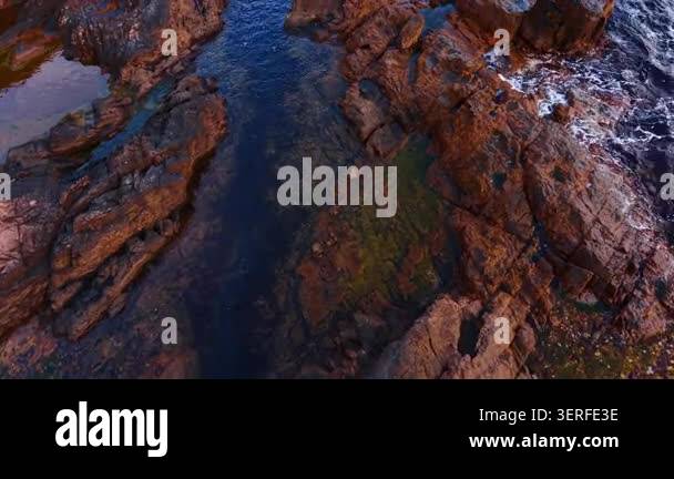 Warm light on wet coastal rock formations with dark sea. Close aerial ...