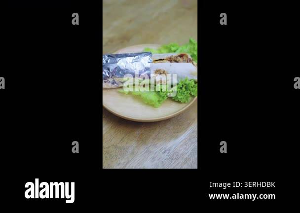 Savory meat wrap or kebab partially wrapped in foil, served on a fresh ...