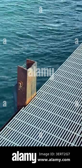 a-metal-post-stands-at-the-edge-of-a-grated-dock-the-surface-is-lined