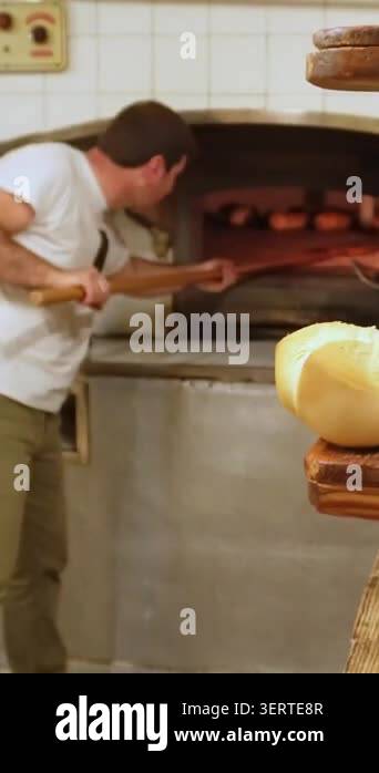 Male baker using a long wooden peel to take out freshly baked loaves of ...