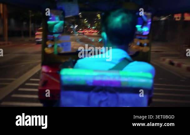 Rear passenger view of asian driver steering tuktuk under neon roof ...