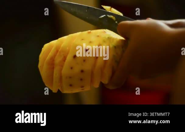 Hands slice a pineapple with care. Golden flesh gleams under warm light ...
