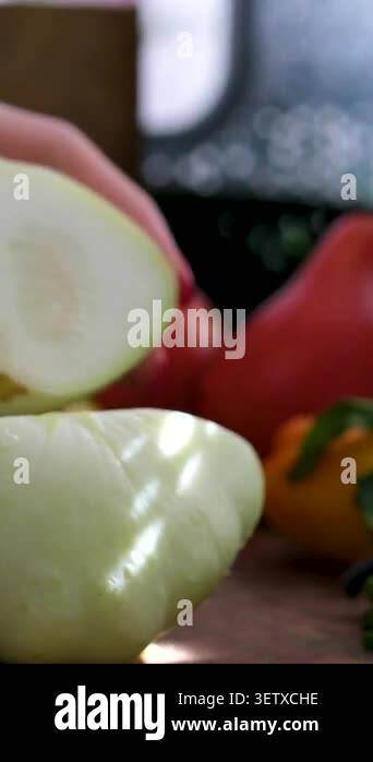 Home kitchen scene where a woman cuts pattypan squash with a big knife ...