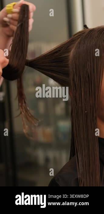 Professional hairstylist twisting a strand of long wet brown hair to ...