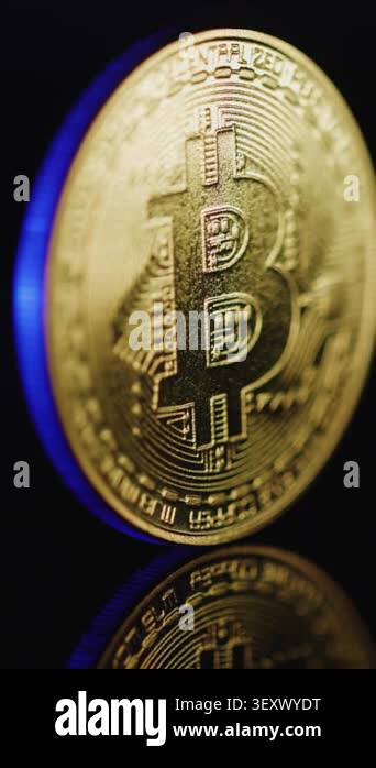 A bitcoin coin shines against a dark background while showing details ...