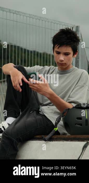 Vertical video of a teenage boy using a smartphone, then putting on a ...