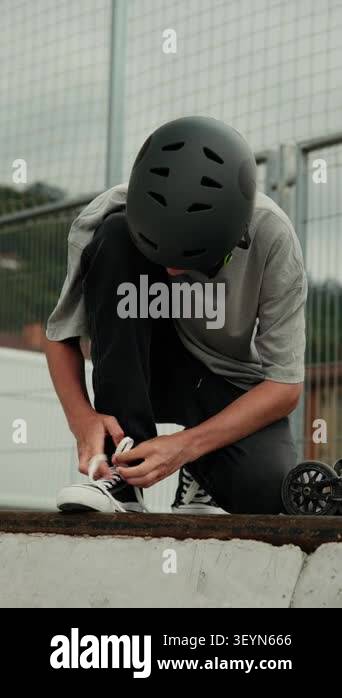 Vertical video of a teenage boy in a helmet tying his shoelaces before ...
