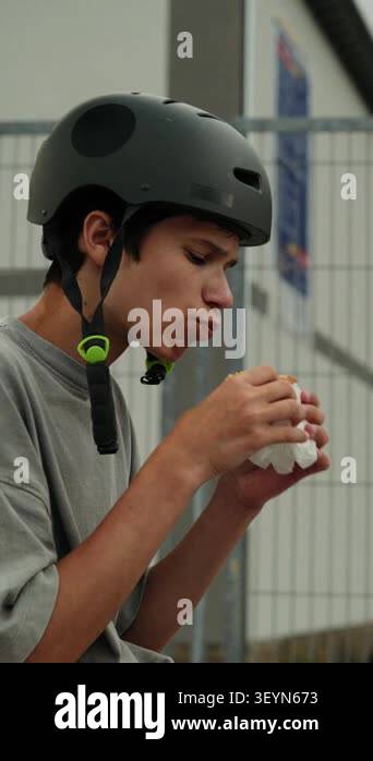 A teenage boy wearing a helmet eats a snack while taking a break at an ...