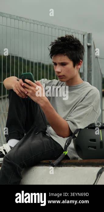 Teenage boy using a smartphone while sitting on a ramp at a skatepark ...