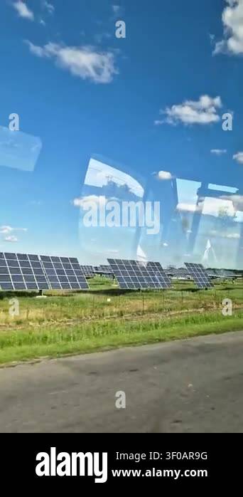 Rows of solar panels stand in a green field under a blue sky seen ...