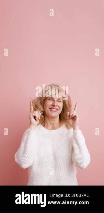 Cheerful senior woman smiling and pointing upwards with both hands ...