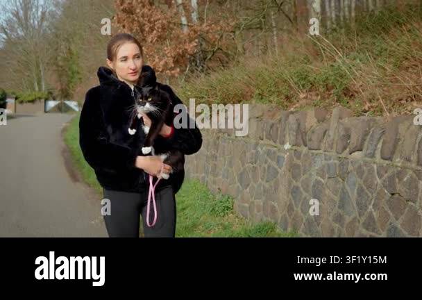 Woman walking along rural road holding domestic cat in arms. Pet owner