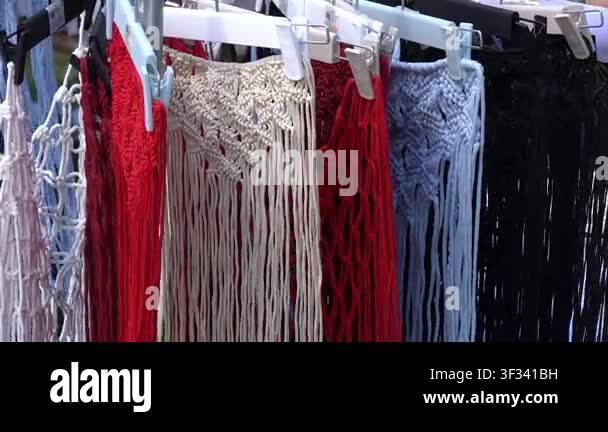 Many fabric items are hanging on a rack at a crafts market. The colors ...