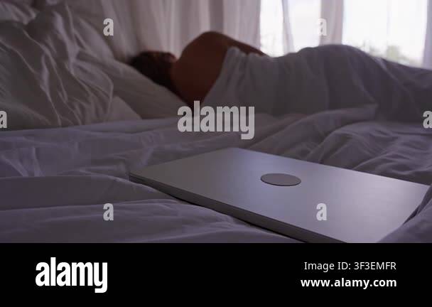 Closed Laptop on Bed Beside Sleeping Woman in Cozy Bedroom with Soft ...