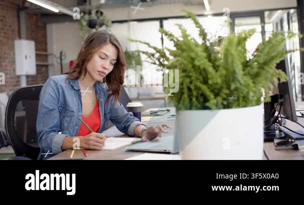 Female business worker writing notes, glancing at laptop, using ...