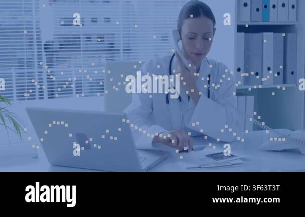 Mid-adult female doctor on phone call, typing updates on laptop, using ...
