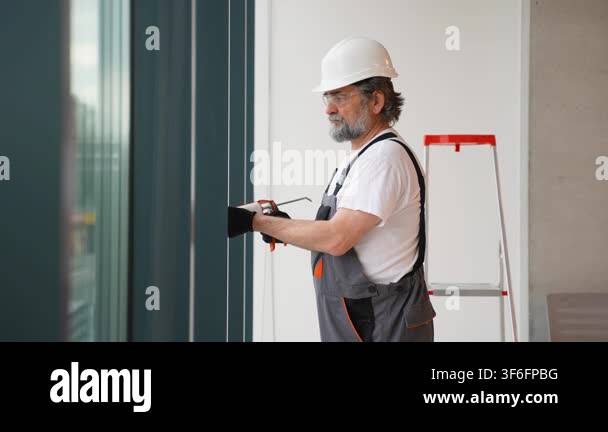 Senior caucasian construction worker in a hard hat applying silicone ...