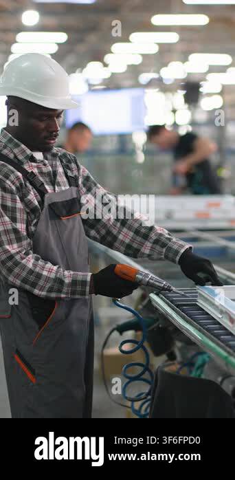 Focused african american worker in a hard hat and overalls using a ...