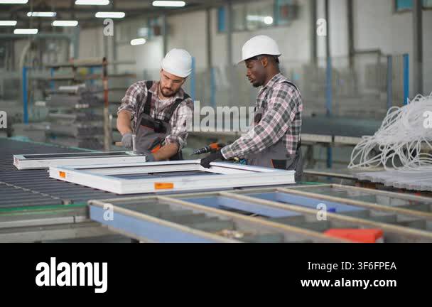 Two diverse factory workers in hard hats and uniforms collaborating on ...