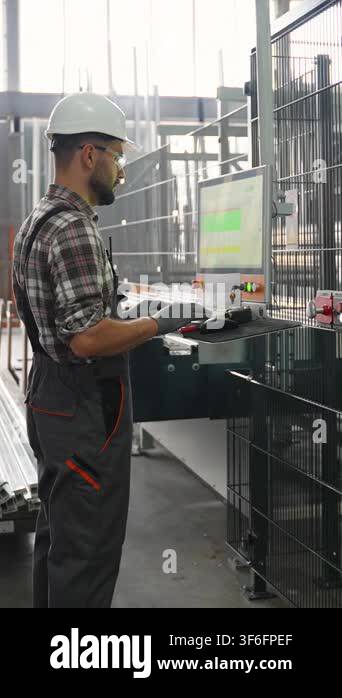 Male factory worker in a hard hat operating a computer controlled ...