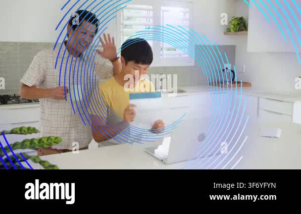 Dad giving teal-header doc to son reviewing on silver laptop for ...