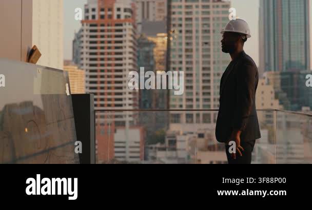 African American construction engineer in a white hardhat surveys ...