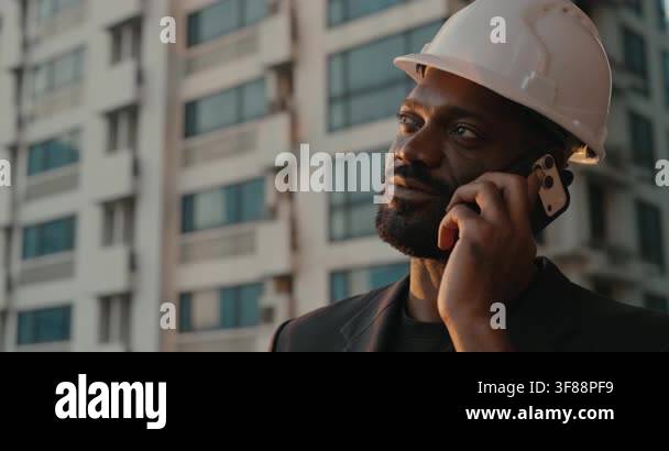 African American construction engineer in a white hardhat talks on a ...