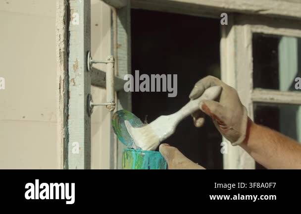Caucasian man in gloves applies paint to a window frame using a brush ...