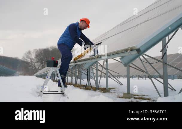 Male engineer in a hard hat installing and adjusting solar panels on a ...