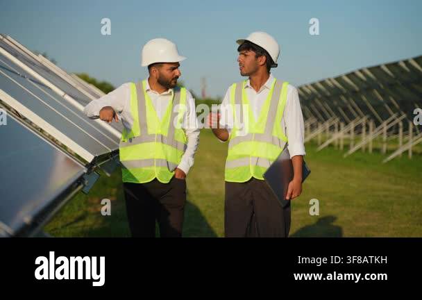 Two male indian engineers in hard hats and safety vests walking and ...