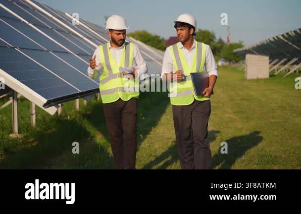Two male indian engineers wearing hard hats and safety vests walking ...