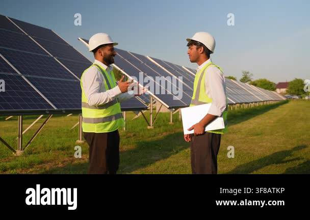 Two multiethnic male engineers in hard hats and safety vests discussing ...