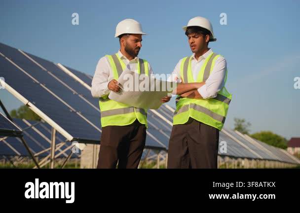 Two male electrical engineers in hard hats and safety vests discussing ...