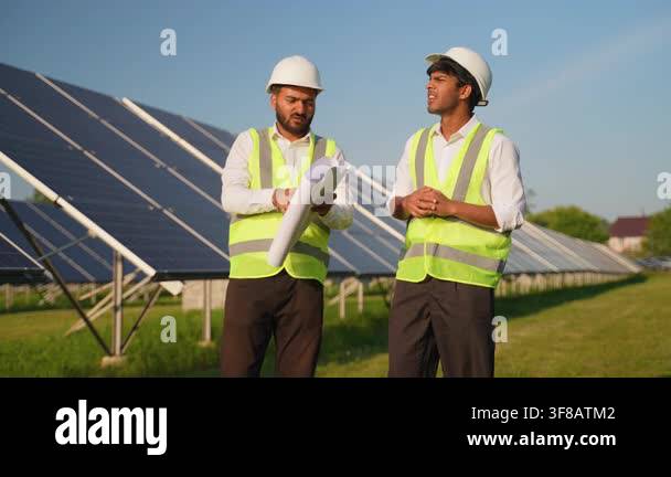 Two male engineers in safety vests and hard hats discussing a project ...