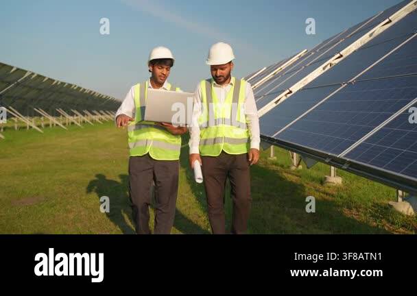 Two male electrical engineers in hard hats and safety vests walking ...