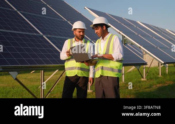 Two dedicated male engineers in hard hats and safety vests discussing a ...