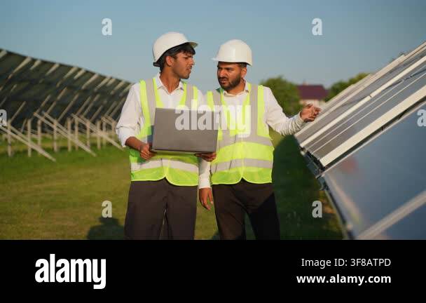 Two male indian engineers wearing safety vests and hard hats discussing ...