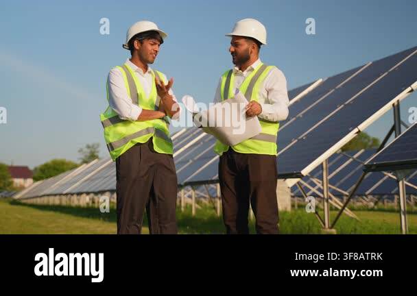 Two multiracial male engineers in safety vests and hard hats discussing ...