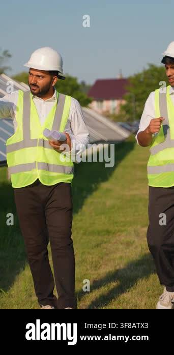 Two engineers wearing hard hats and safety vests walking and talking ...