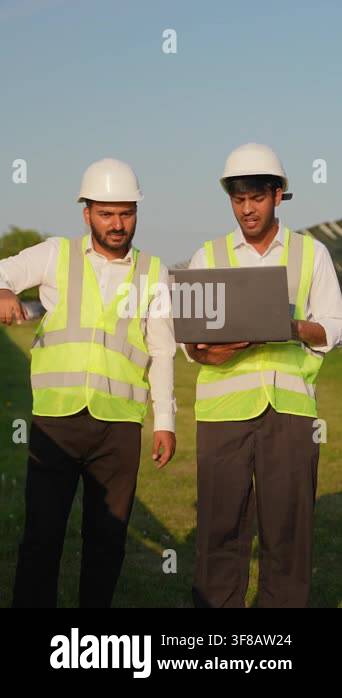 Two diverse solar energy technicians wearing hard hats and safety vests ...