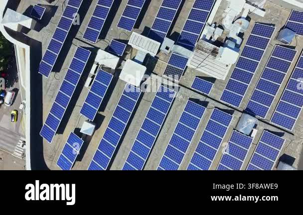 Rows of solar panels are arranged on a rooftop in a city. The sun ...