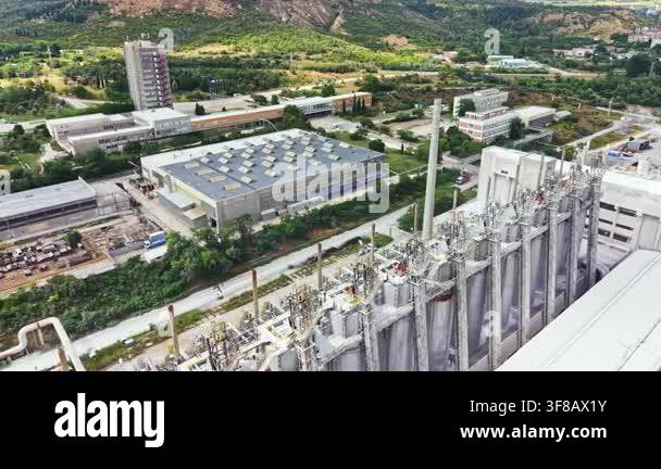 Factories and silos are seen in the foreground with green hills and ...