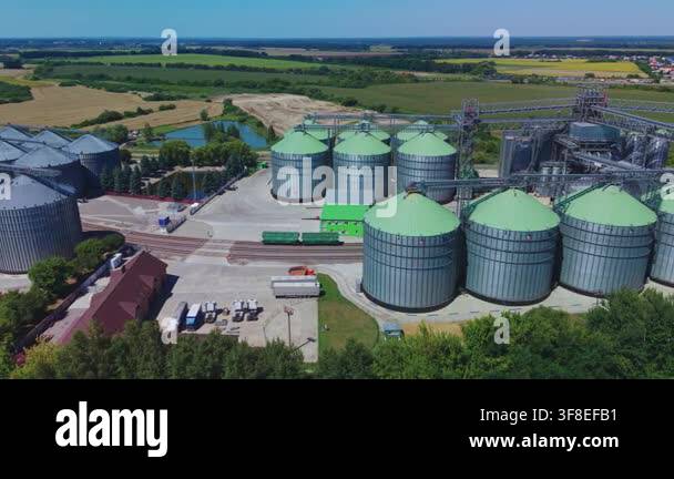 Dynamic aerial overview shows large silver and green metal silos of ...