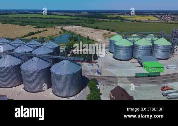 Dynamic aerial overview reveals rows of silver and green metal silos at ...