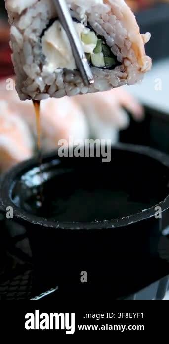 Fresh shrimp sushi roll held with metal chopsticks dipping into soy ...