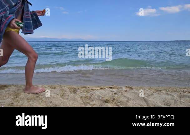 person-walks-barefoot-on-sandy-beach-near-ocean-waves-blue-sky-with